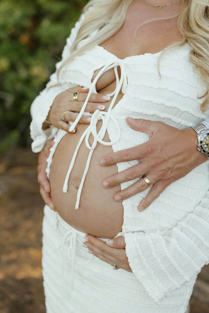 Close up of married couple's hands holding wife's pregnant belly in Lake Tahoe