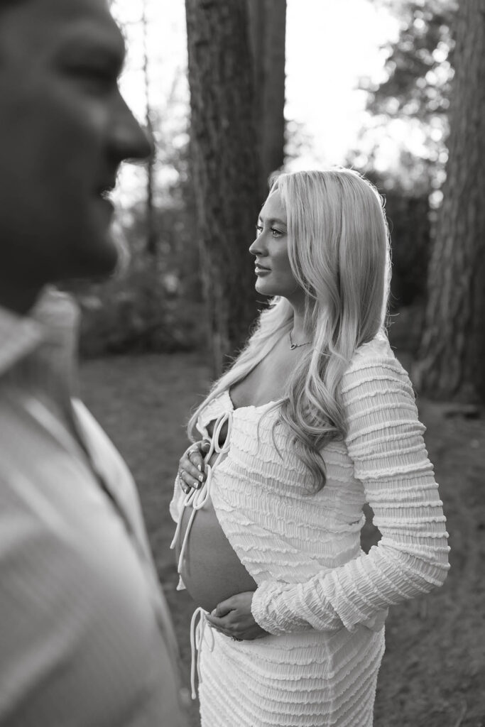 Pregnant wife holding belly while looking out in distance next to husband in Lake Tahoe