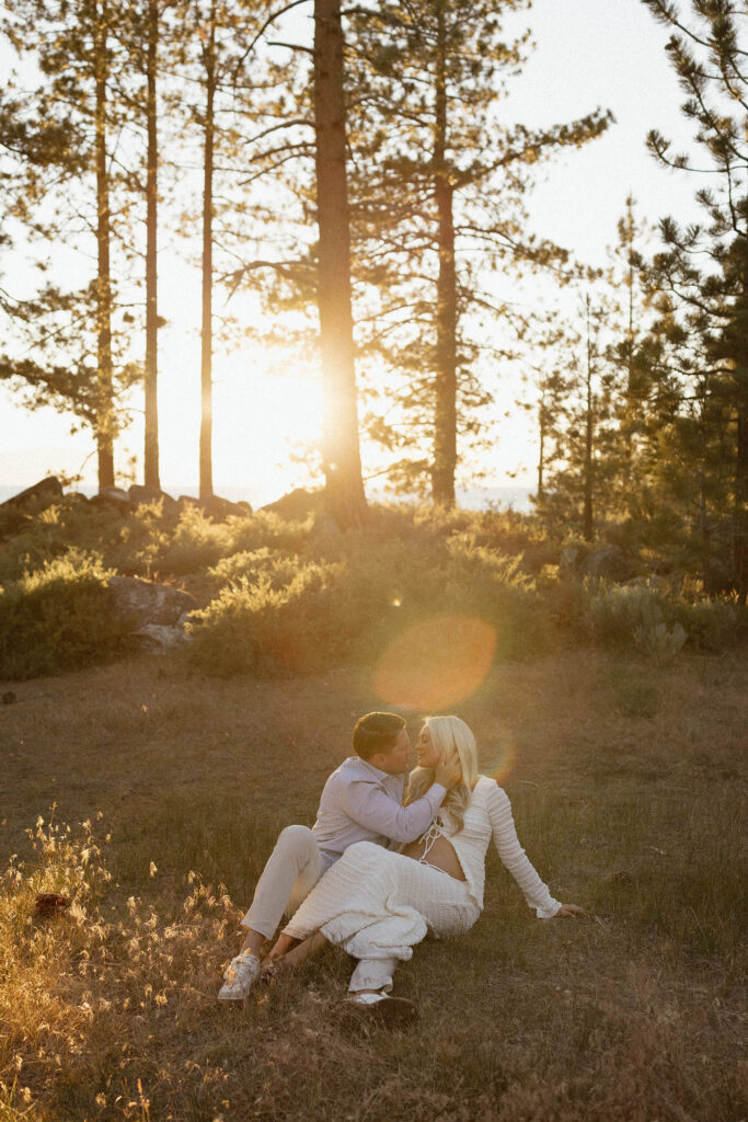 Married couple sitting together in grass and kissing with sunset in background in Lake Tahoe