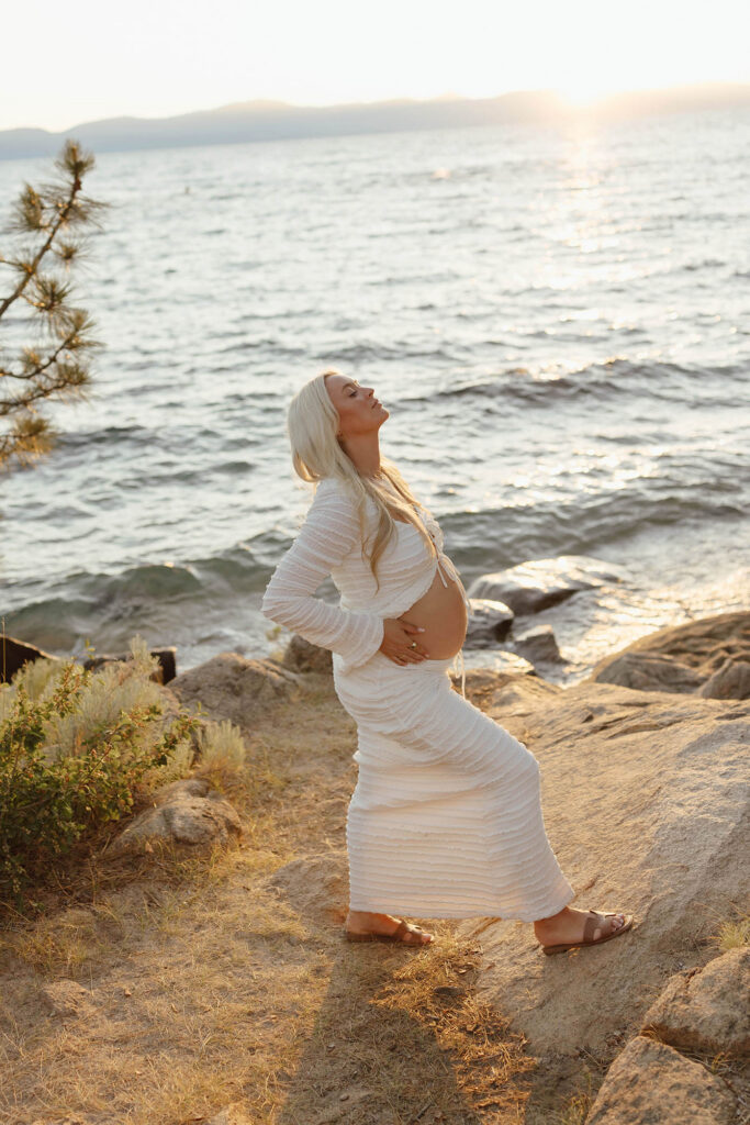 Pregnant wife on a beach at Lake Tahoe and showing off her belly in white maternity attire