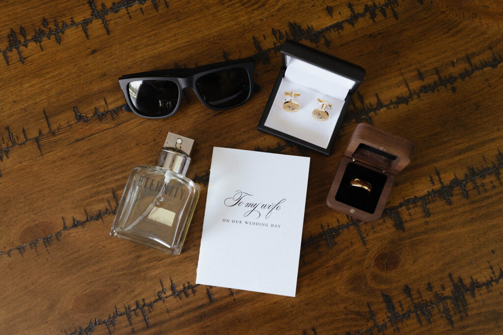 Wedding details in flat lay with golden ring and cuff links on wooden floor at Kinship Ranch