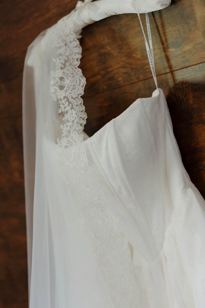Close up of wedding dress and veil hanging on hanger on wooden wall at Kinship Ranch