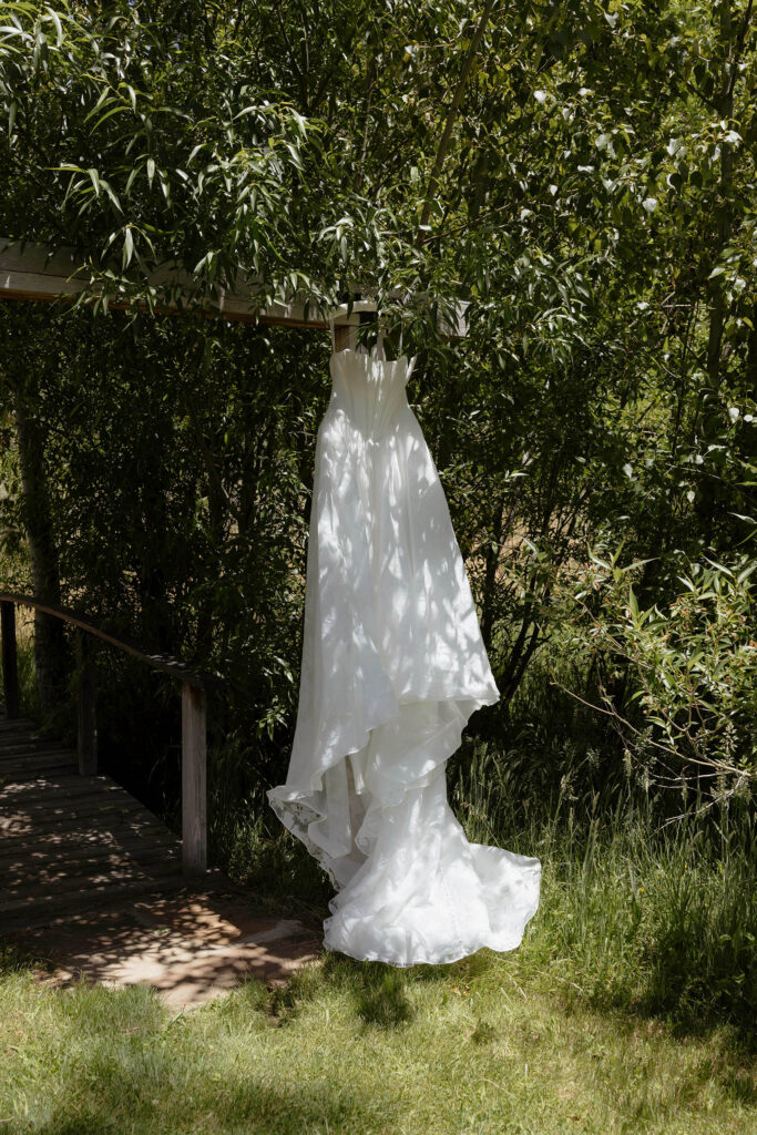 Bride's wedding dress hanging on hanger in between greenery at Kinship Ranch