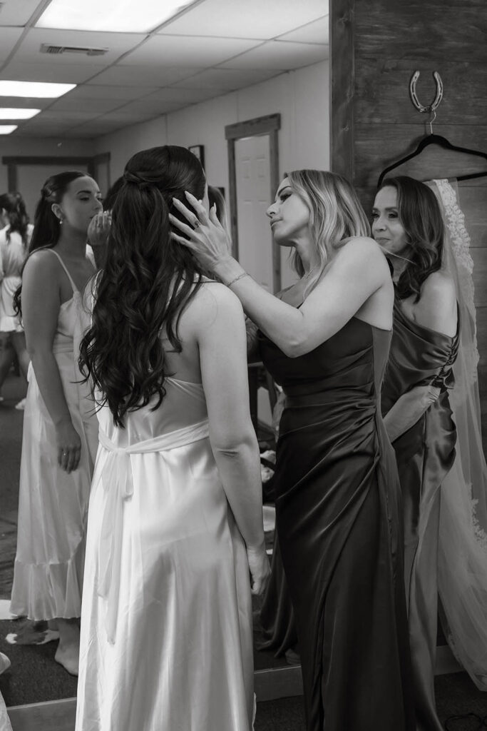 Wedding bridesmaid helping bride with makeup while getting ready inside at Kinship Ranch