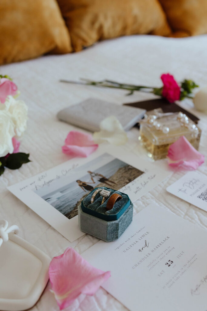 Wedding rings displayed beside invitations, perfume, rose petals, and floral details for a Lake Tahoe elopement