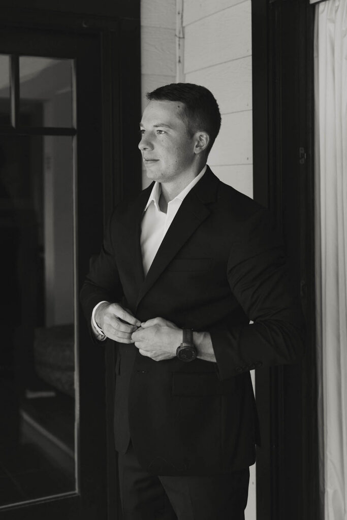Black-and-white portrait of the groom buttoning his suit before his Lake Tahoe elopement