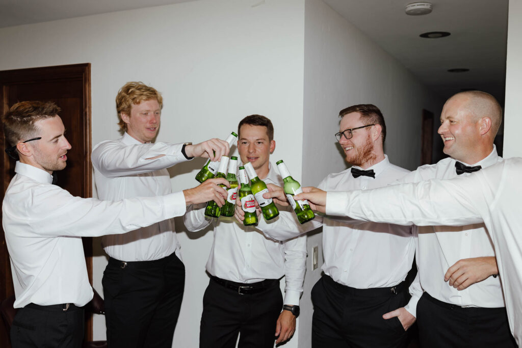 Groom and groomsmen celebrating with a beer toast before the Emerald Bay ceremony