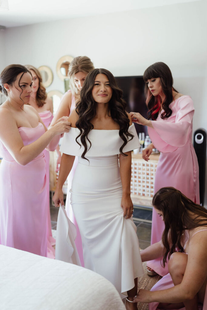 Bridesmaids in pink dresses help the bride into her wedding gown before their Emerald Bay ceremony