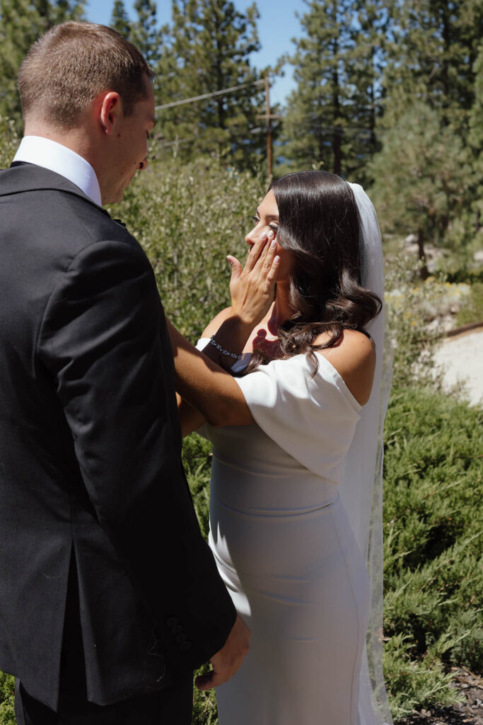 The bride wipes away tears while seeing the groom during their emotional Lake Tahoe first look