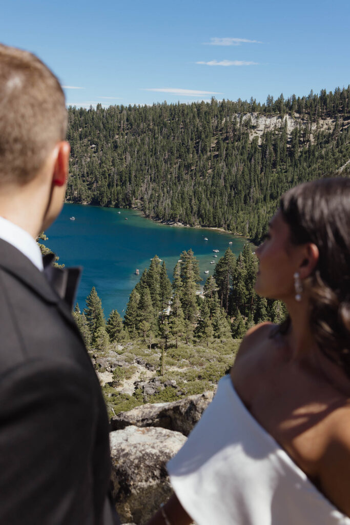 The bride and groom admire the turquoise water and pine-covered shoreline of Emerald Bay in Lake Tahoe