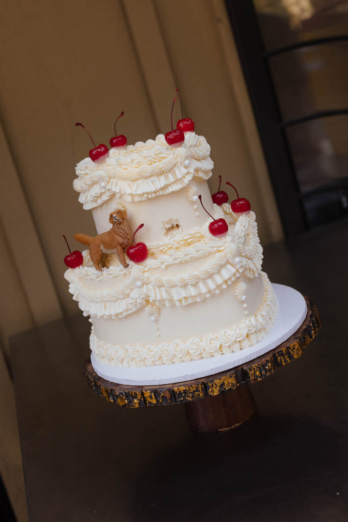 Two-tier vintage-style wedding cake decorated with cherries and a golden retriever topper