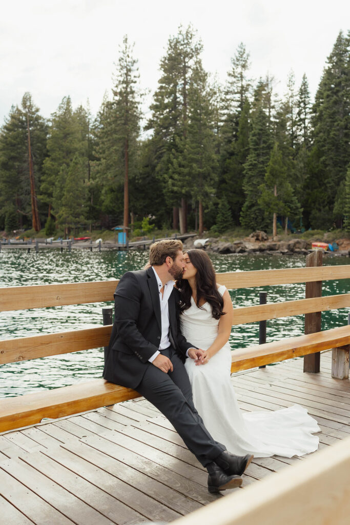 Bride and groom kiss while sitting on a wooden dock at Lake Tahoe