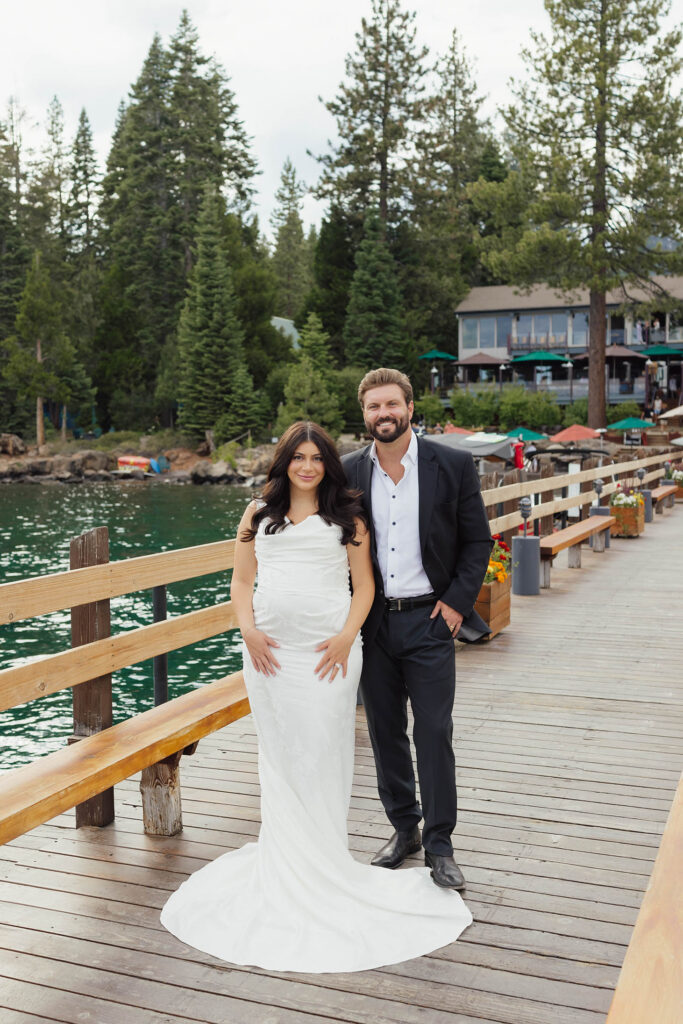 Bride and groom pose together on a lakeside dock surrounded by pine trees