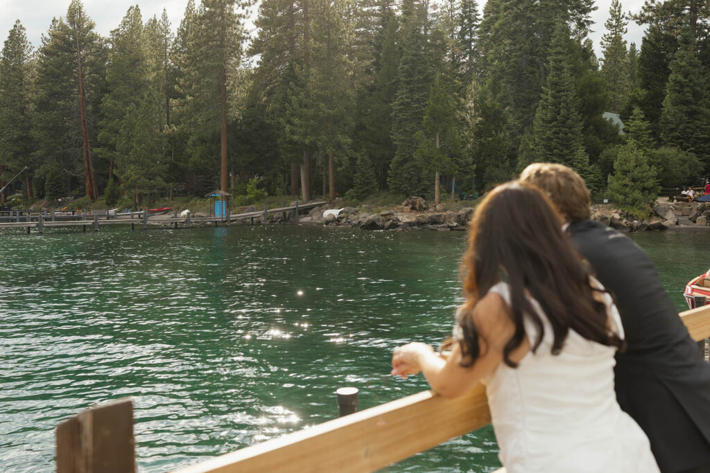 Bride and groom leaning against a dock railing overlooking the sparkling lake