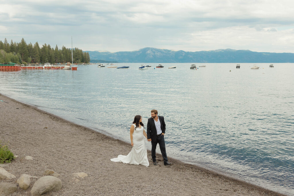 Elopement couple hold hands on the shore with Lake Tahoe and mountains behind them