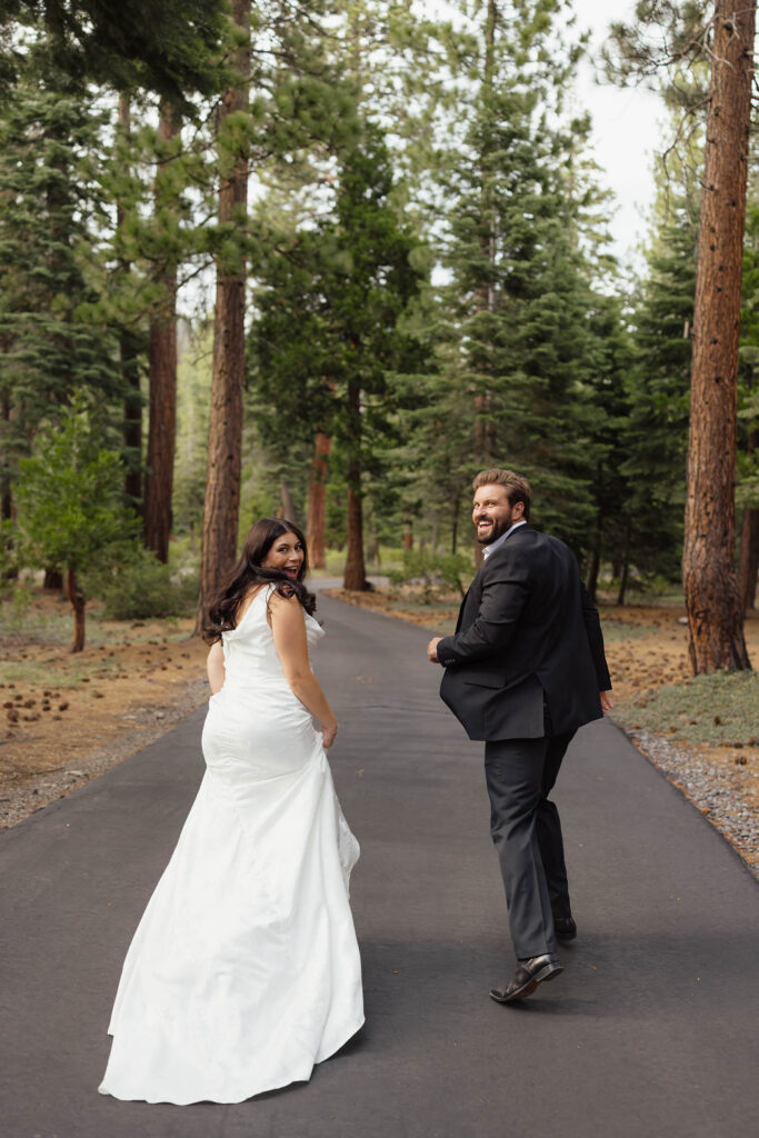 Bride and groom look back laughing while walking through the forest in Lake Tahoe