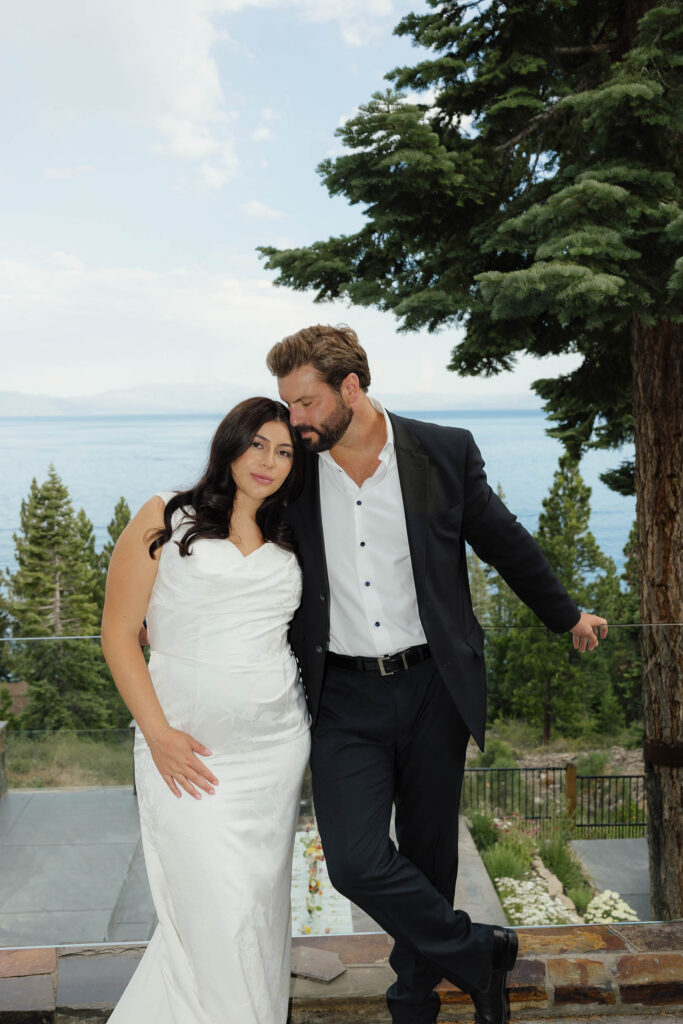 Elopement couple hug beneath a pine tree with Lake Tahoe in the background while the bride looks at the camera and the groom looks at her