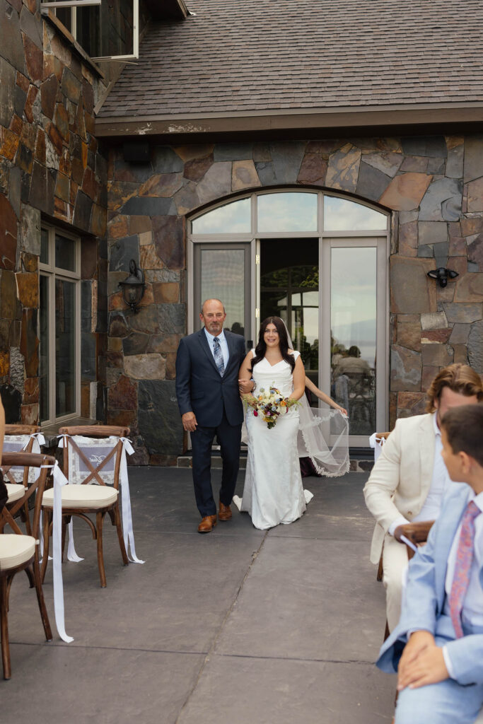 Bride walks down the outdoor aisle at Airbnb with her father while holding a colorful bouquet in Lake Tahoe