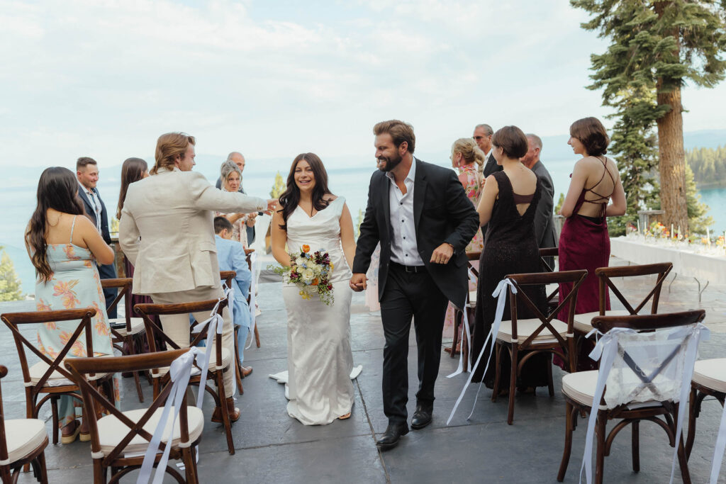 Newlyweds smile and hold hands while walking back down the aisle after their Lake Tahoe ceremony