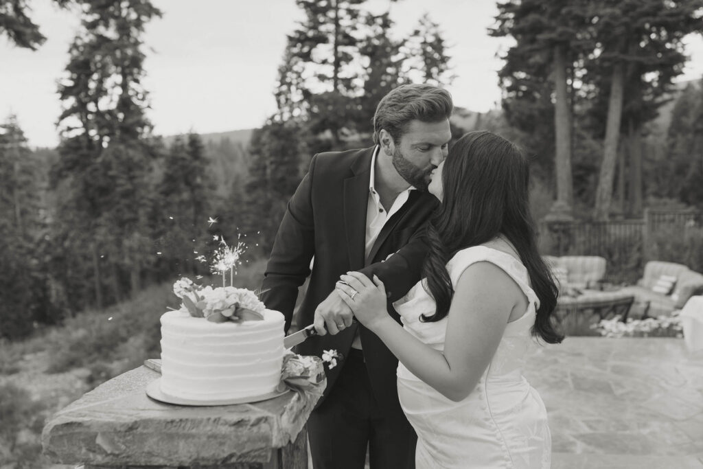 Black and white photo of the newlyweds kissing while cutting their wedding cake with sparklers on it