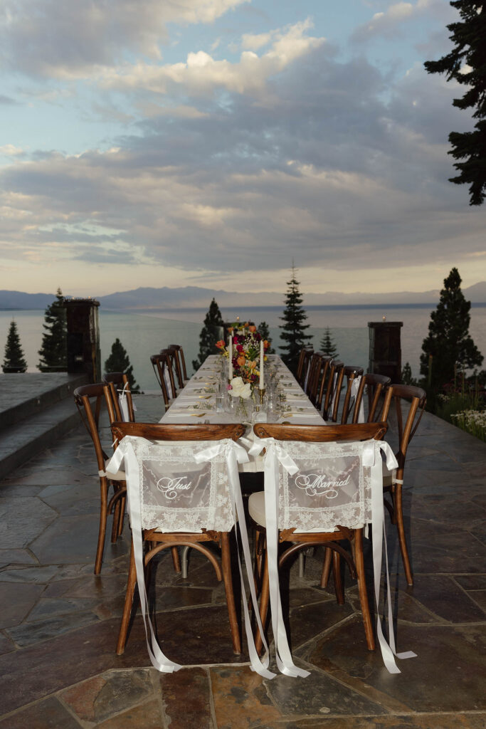 Lakeside reception table with candles, flowers, and “Just Married” chair signs in Lake Tahoe at sunset