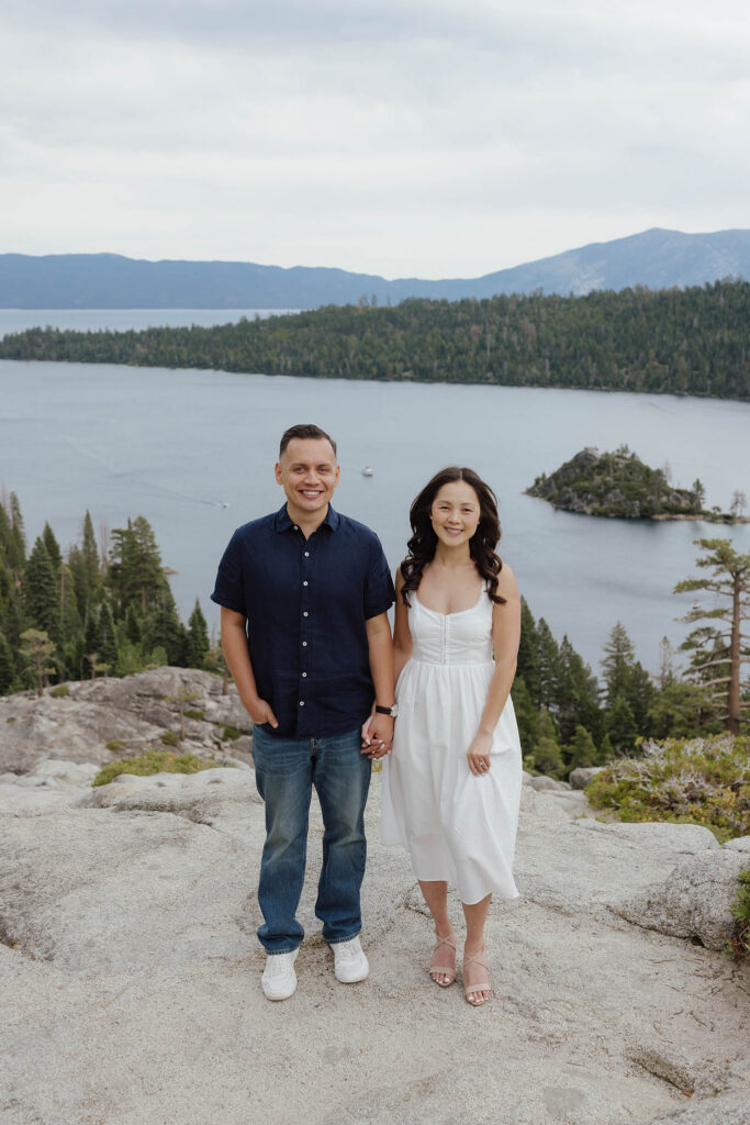 Engagement couple holding hands while smiling at camera together with Emerald Bay in background