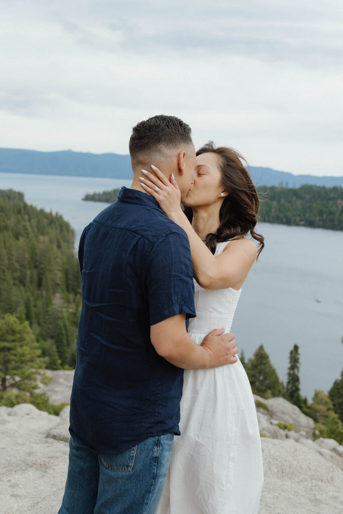 Engagement couple holding each other and kissing with Emerald Bay and mountains in background