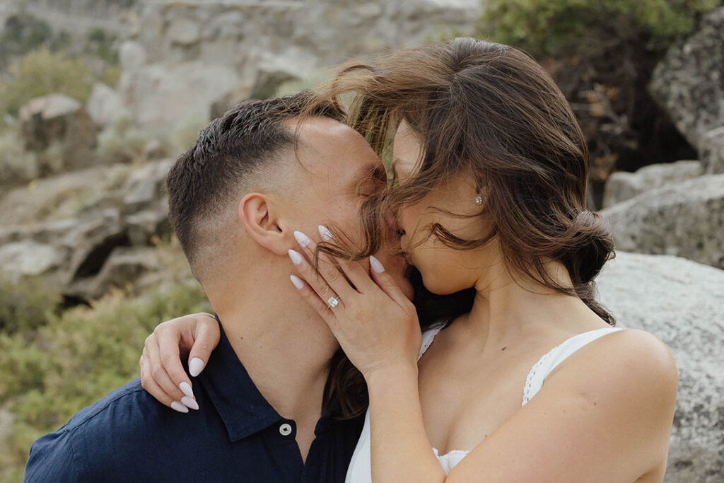 Close up of engagement couple kissing with woman's hand on fiancé's face wearing engagement ring at Emerald Bay