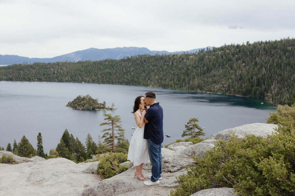 Engagement couple kissing while holding each other with great view of Emerald Bay behind them