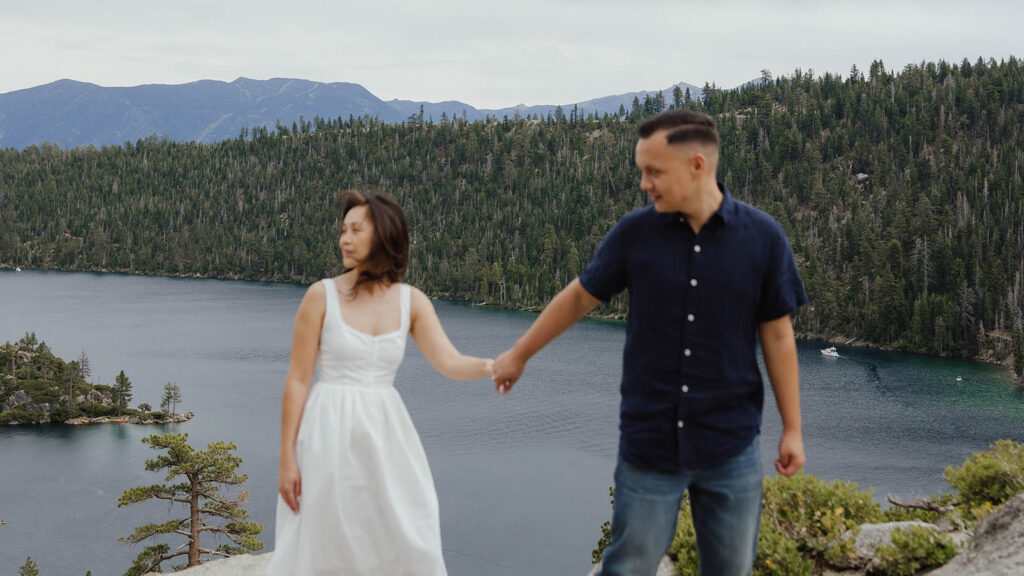 Engagement couple walking while holding hands with Emerald Bay in background