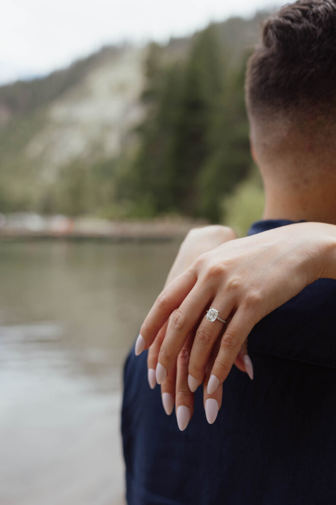 Close up of woman's hands draped over fiancé while wearing engagement ring at Emerald Bay