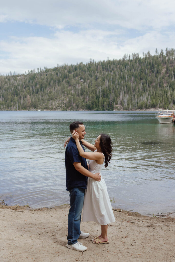 Engagement couple holding and smiling at each other while standing on a beach at Emerald Bay