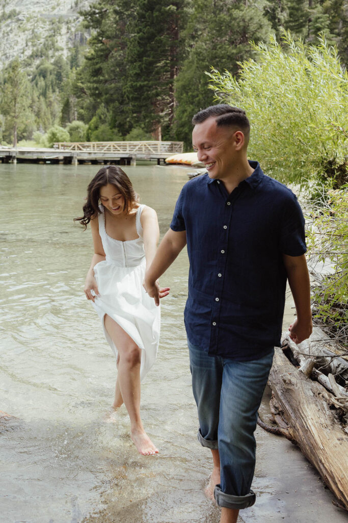 Engagement couple holding hands and walking through water together on a beach in Emerald Bay