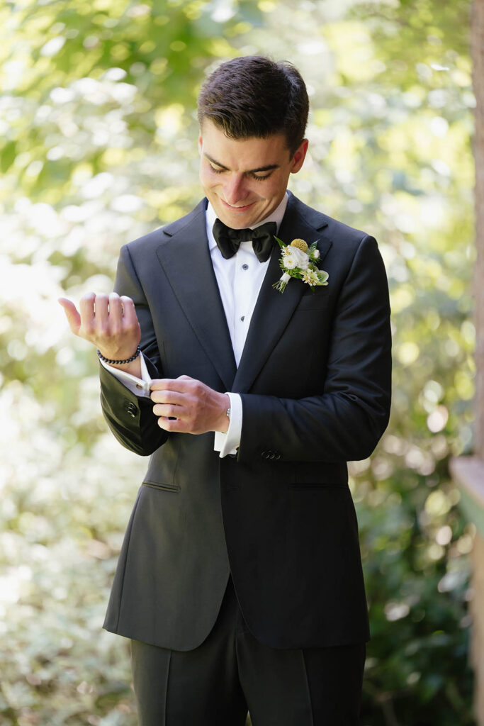 Groom smiles while adjusting his cuff during his summer wedding preparations