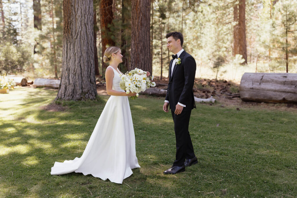 Bride and groom smile during their first look beneath the Lake Tahoe pine trees
