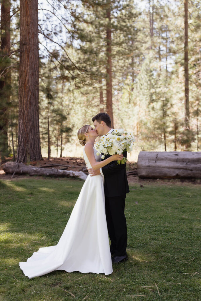 Bride and groom kiss beneath the pine trees during their summer wedding at Valhalla Tahoe