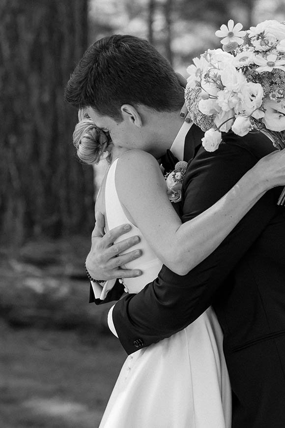 Black-and-white photo of the newlyweds embracing with the bride’s bouquet over the groom’s shoulder