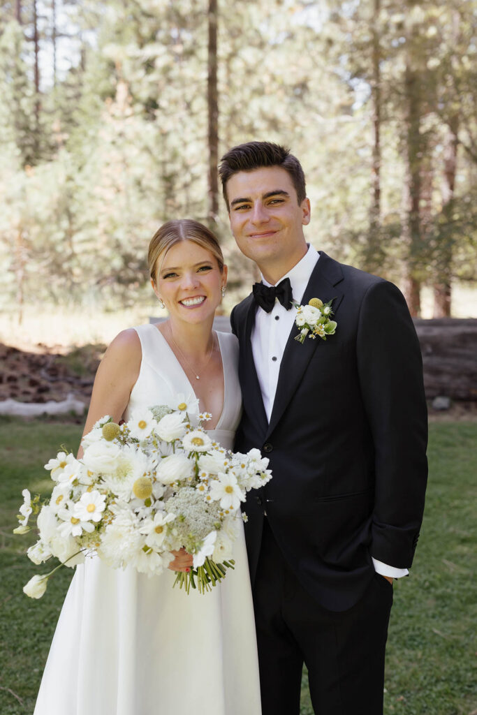 Bride and groom smile together while holding a large white floral bouquet