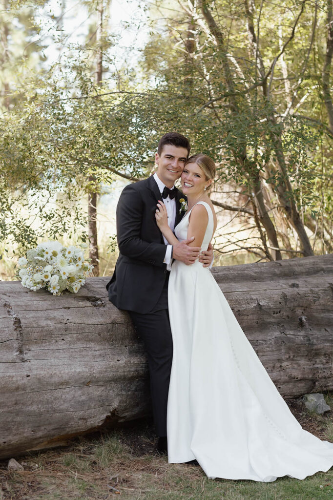 Newlyweds embrace beside a fallen tree in the Lake Tahoe forest