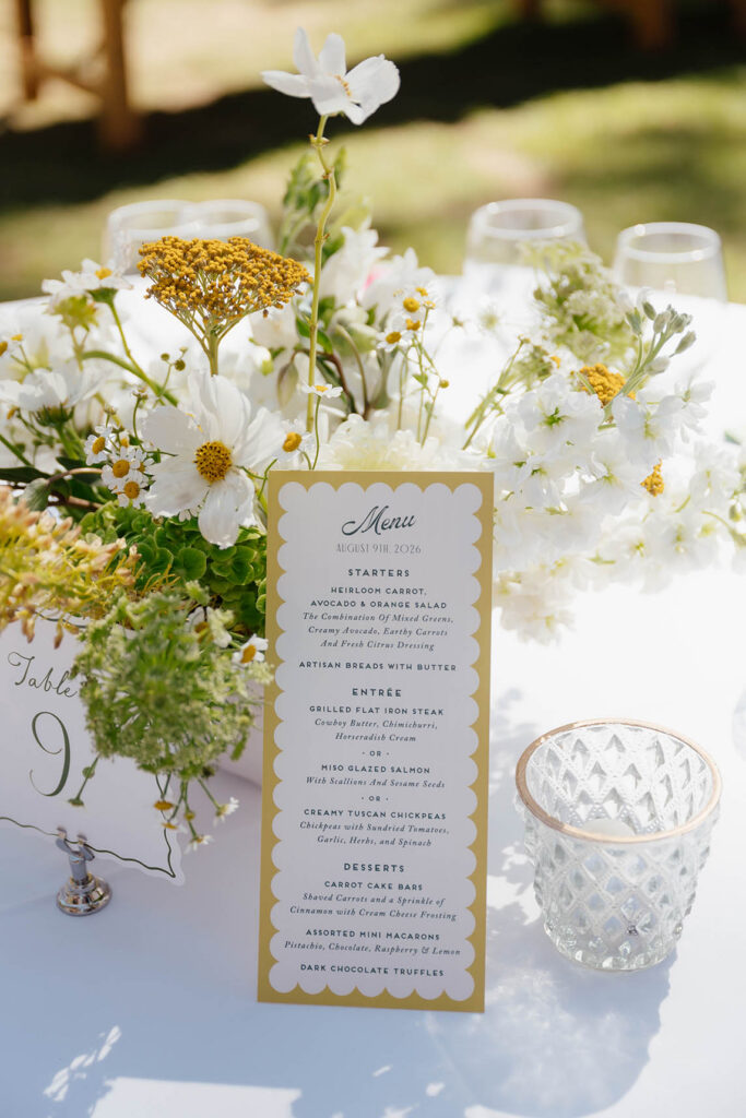 Summer wedding menu displayed among white and yellow floral arrangements