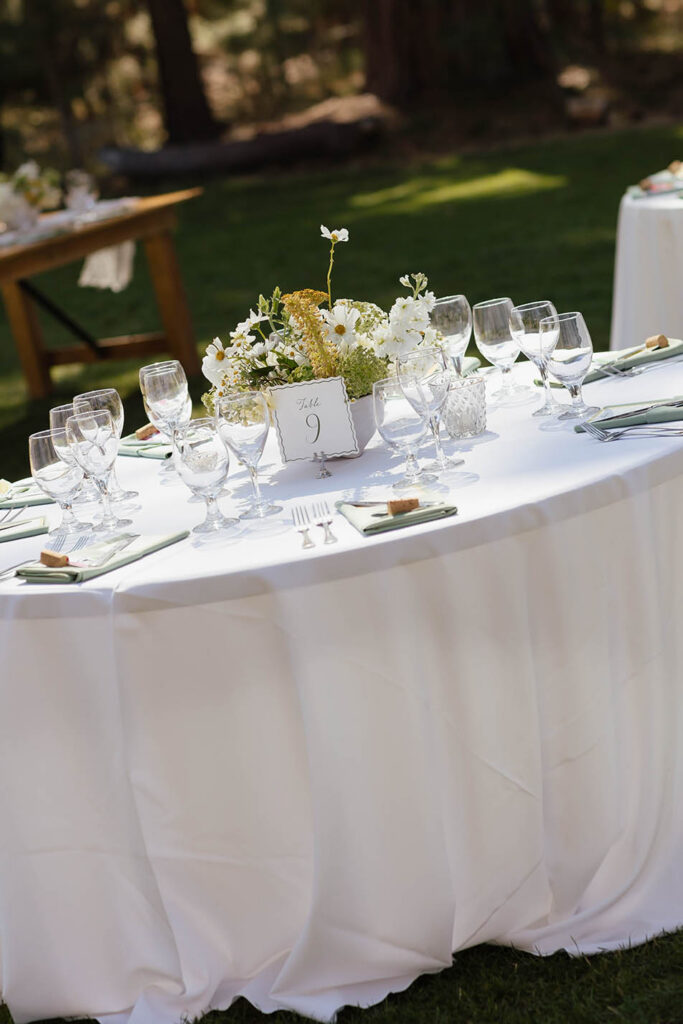 Reception table set with white linens, glassware, green napkins, and wildflowers