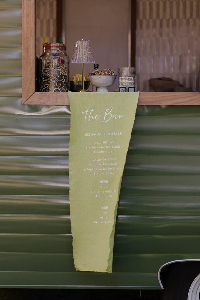 Green mobile bar with a fabric menu listing signature wedding cocktails