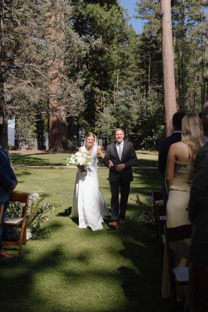 Bride and her father enter the forest ceremony surrounded by standing wedding guests
