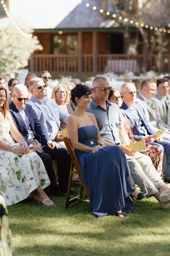 Wedding guests watch the outdoor summer ceremony beneath the pine trees