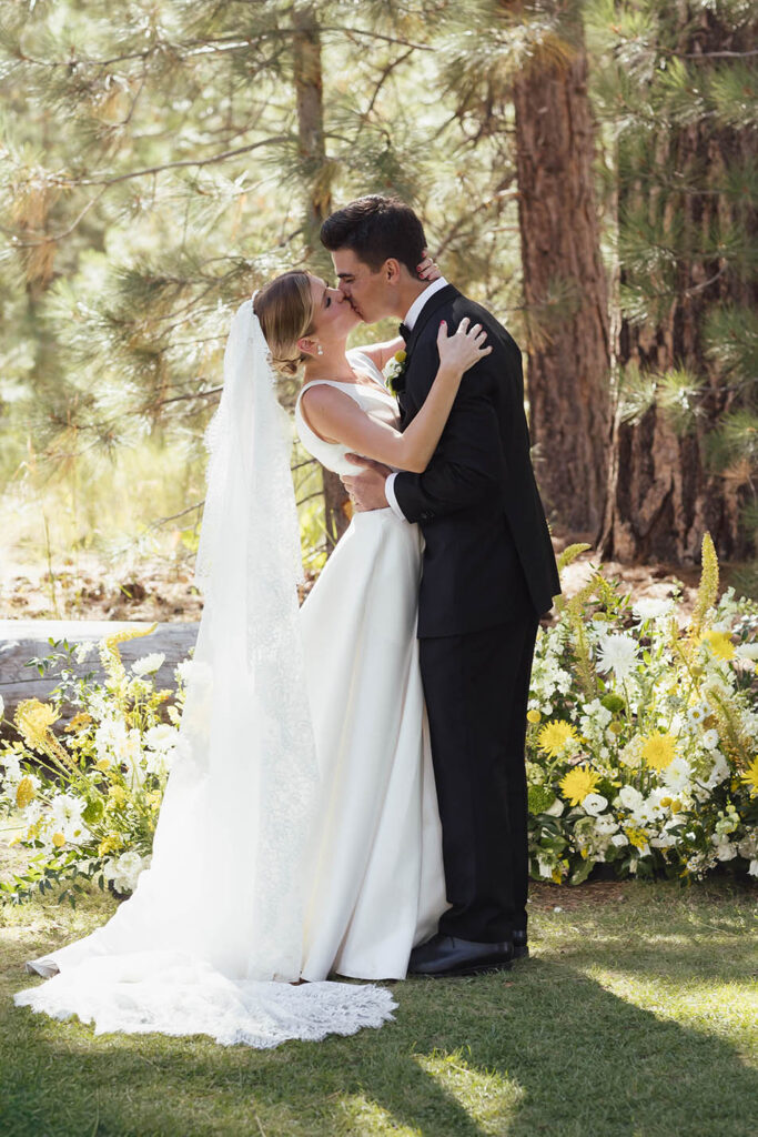 Bride and groom share their first kiss surrounded by white and yellow flowers