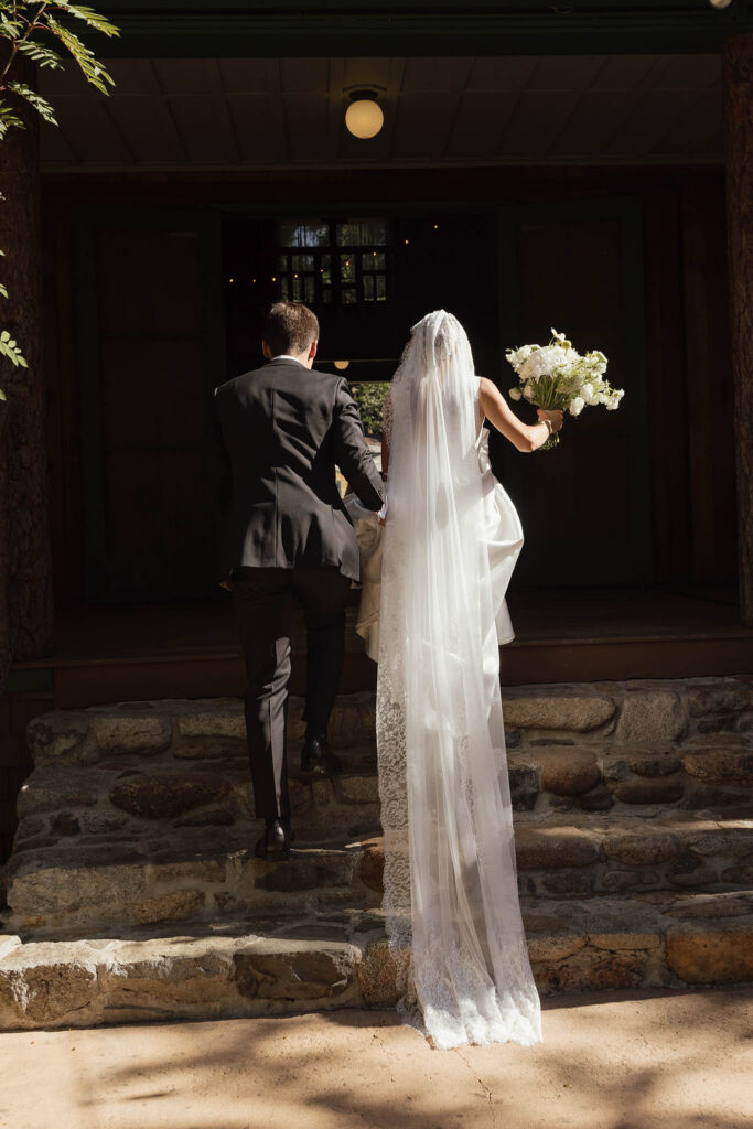 Newlyweds climb the cabin steps with the bride’s long lace veil trailing behind them