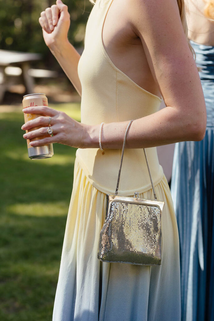 Wedding guest in a yellow dress carries a sparkling silver purse and canned drink