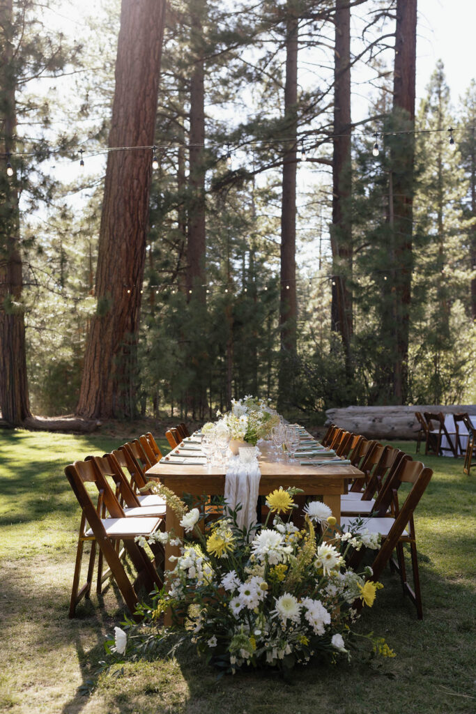 Wooden head table decorated with white and yellow wildflowers beneath string lights