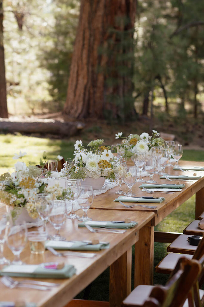 Outdoor reception table set with green napkins, glassware, and summer wildflowers