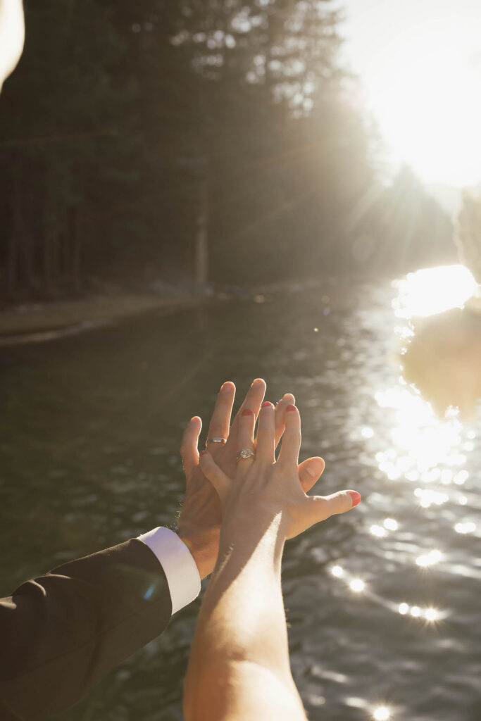 Newlyweds show their wedding rings against the sunlit waters of Lake Tahoe